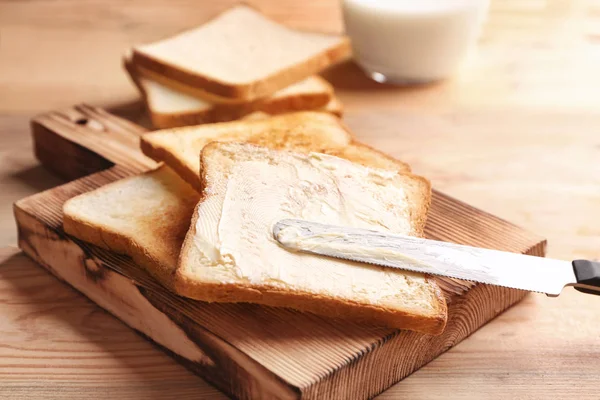 Wooden board with tasty toasted bread and butter on table — Stock Photo, Image