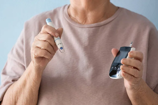 Ältere diabetische Frau mit Lanzettstift und Glukometer auf farbigem Hintergrund, Nahaufnahme — Stockfoto