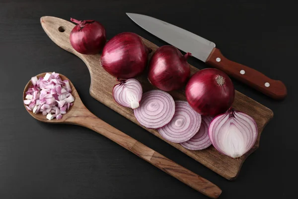 Tablero de madera con corte y cebollas rojas enteras sobre fondo negro — Foto de Stock