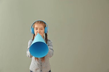 Little girl with headphones and paper megaphone on color background clipart