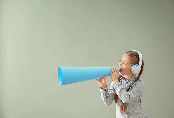 Meisje met hoofdtelefoons en papier megafoon op kleur achtergrond — Stockfoto