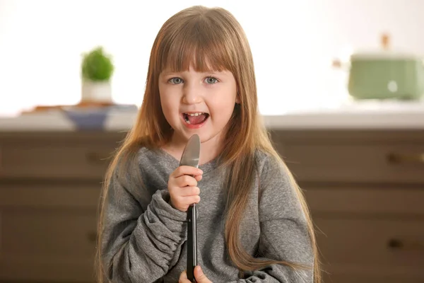 Милая маленькая девочка использует ложку в качестве микрофона дома — стоковое фото