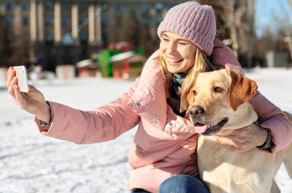 Woman taking selfie with cute dog outdoors on winter day