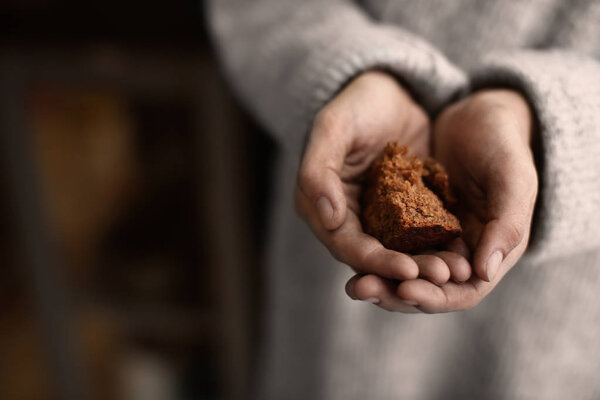 Poor woman holding piece of bread on blurred background