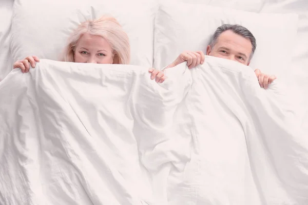 Casal sênior escondido sob cobertor na cama juntos, vista superior — Fotografia de Stock