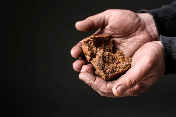 Povero uomo che tiene pezzi di pane su sfondo scuro — Foto Stock