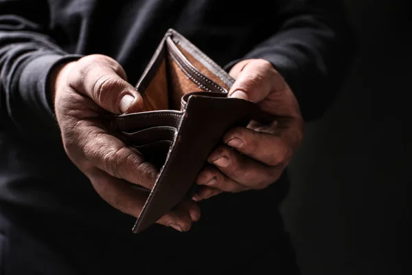 Armer Mann zeigt sein leeres Portemonnaie auf schwarzem Hintergrund — Stockfoto