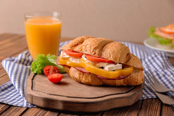 Välsmakande croissant smörgås och ett glas juice serveras till frukost på bordet — Stockfoto