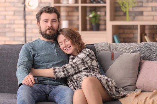 Happy couple watching TV while sitting on sofa at home — Stock Photo, Image