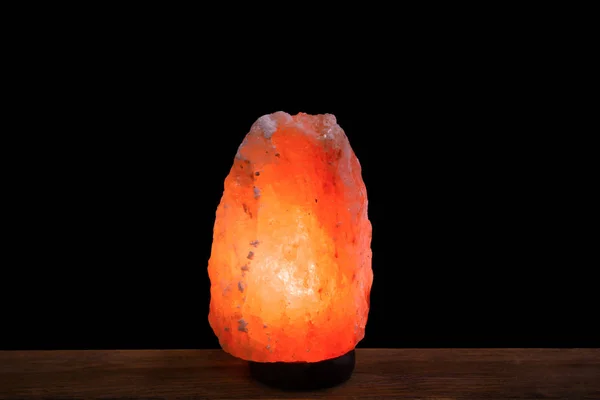 Himalayan salt lamp on table against dark background — Stock Photo, Image