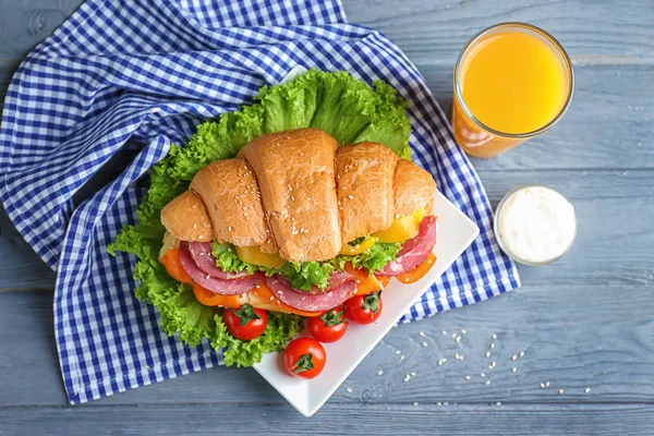 Tallrik med välsmakande croissant smörgås och glas saft på bord — Stockfoto