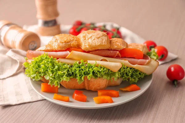 Placa com saboroso sanduíche croissant na mesa — Fotografia de Stock