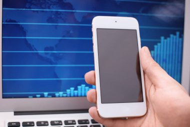 Hisse senedi grafiği veri üstünde perde ile bilgisayarın yakınında Smartphone kullanan adam. Forex kavramı