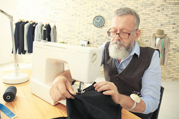 Старший портной работает на швейной машине в ателье
