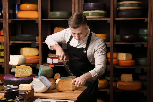Young worker cutting cheese in shop