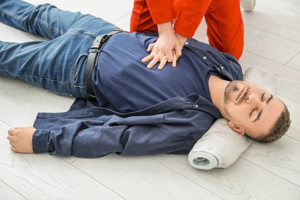 Ung kvinna ger första hjälpen till medvetslösa mannen på golvet, inomhus — Stockfoto