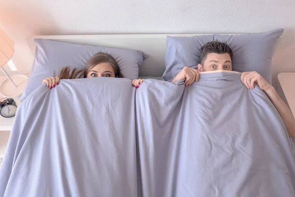 Młoda para ukrywa się pod koc na łóżko w domu — Zdjęcie stockowe