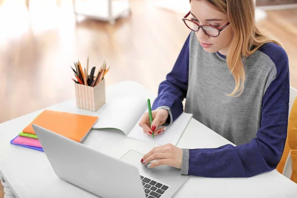 Mooie student met laptop studeren aan tafel binnenshuis — Stockfoto