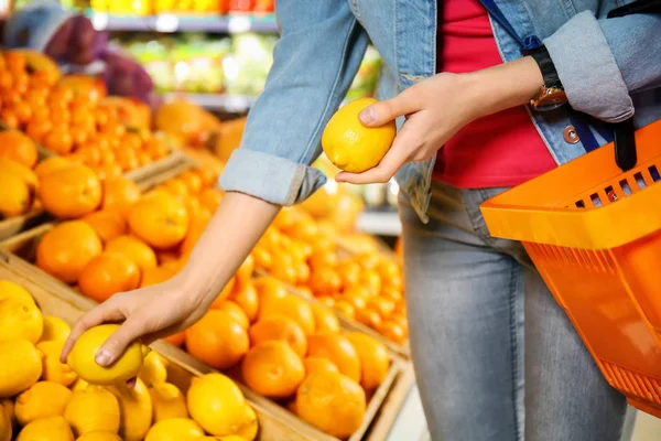 Jeune femme choisissant citrons frais au supermarché — Photo