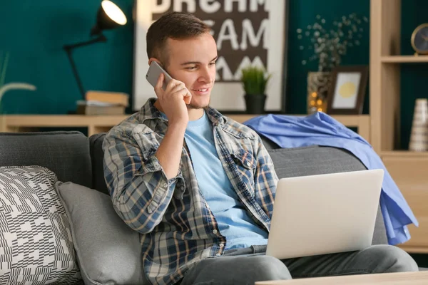Ung man pratar telefonen medan du arbetar med laptop inomhus — Stockfoto