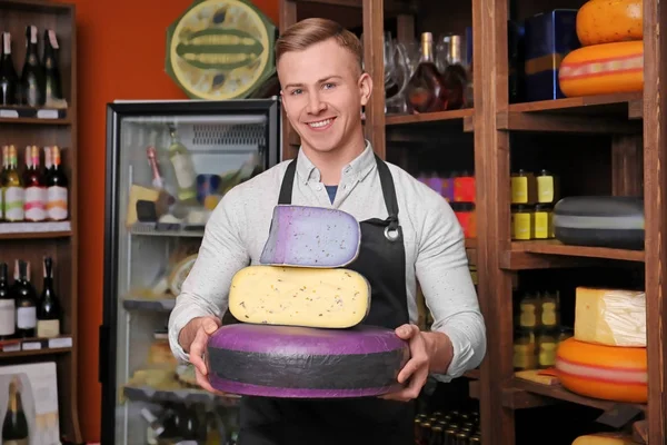 Young worker holding different cheeses in shop