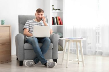 Cep telefonu ile dizüstü evde çalışırken konuşan genç adam