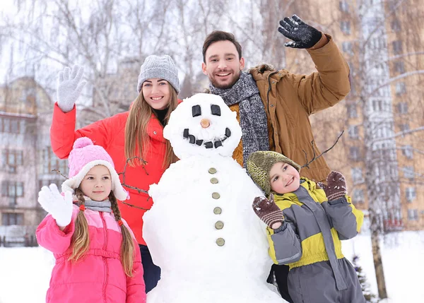 Šťastná rodina s sněhulák v parku na zimní dovolenou — Stock fotografie