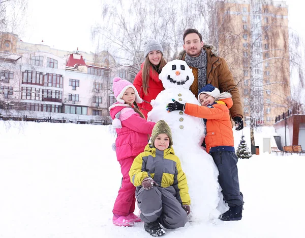 Glückliche Familie mit Schneemann im Park im Winterurlaub — Stockfoto