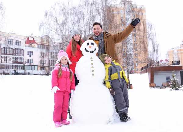 Glückliche Familie mit Schneemann im Park im Winterurlaub — Stockfoto