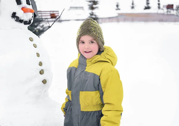 Cute boy with snowman in park on winter vacation — Stock Photo, Image