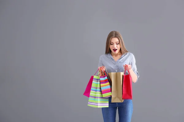 Emocjonalne, młoda kobieta, patrząc wewnątrz torby na zakupy na szarym tle — Zdjęcie stockowe