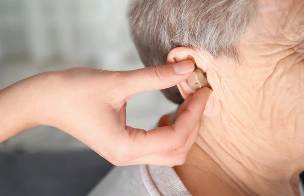 Γιατρός βάζοντας ακουστικό βαρηκοΐας στο αυτί ανωτέρων γυναίκας σε εσωτερικούς χώρους — Φωτογραφία Αρχείου