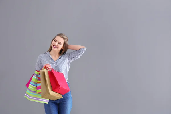 Bella giovane donna con borse della spesa su sfondo grigio — Foto Stock