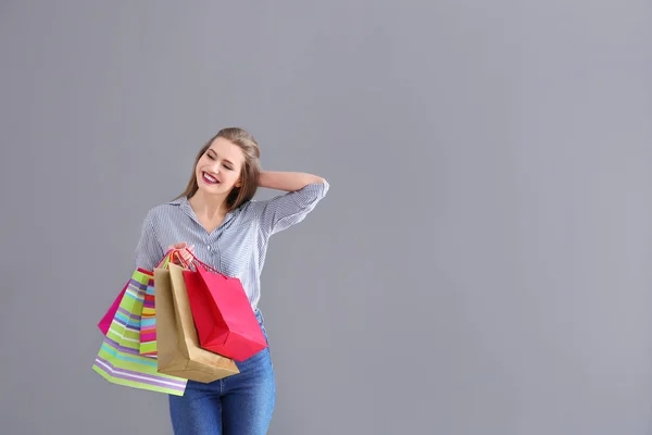 Hermosa mujer joven con bolsas de compras sobre fondo gris —  Fotos de Stock