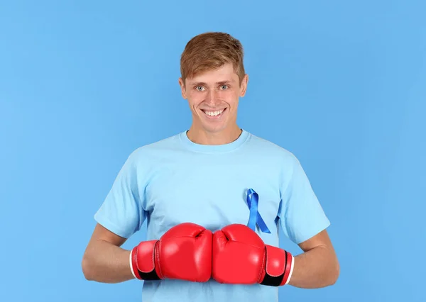 Młody człowiek w t-shirt, z niebieską wstążką na sobie rękawice bokserskie na kolor tła. Koncepcja świadomości raka prostaty — Zdjęcie stockowe