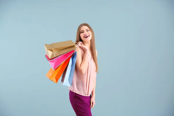 Hermosa mujer joven con bolsas de compras en el fondo de color — Foto de Stock