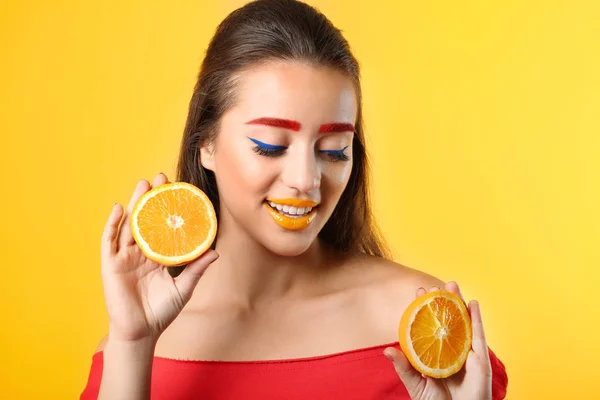 Junge Frau mit gefärbten Augenbrauen und Orangenhälften auf farbigem Hintergrund — Stockfoto
