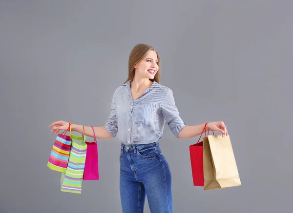 Gyönyörű fiatal nő, bevásárló táskák, a szürke háttér — Stock Fotó