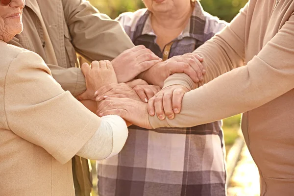 Senior people from care home putting hands together as symbol of unity outdoors — Stock Photo, Image