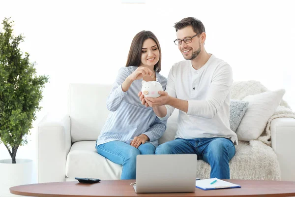 Pareja joven poniendo moneda en alcancía en casa. Pensando en el plan de pensiones —  Fotos de Stock