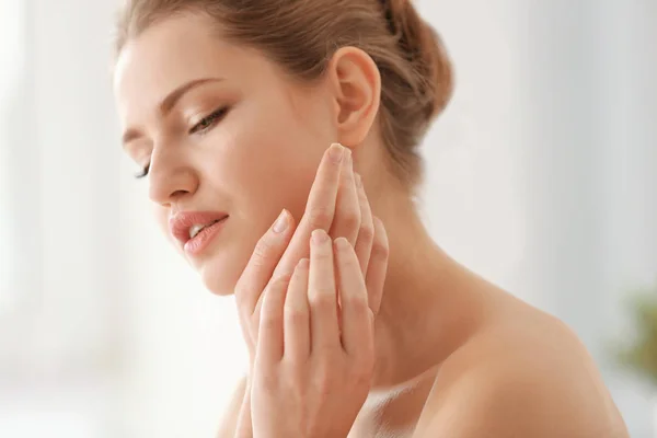 Young woman applying cream onto her skin on light background — Stock Photo, Image