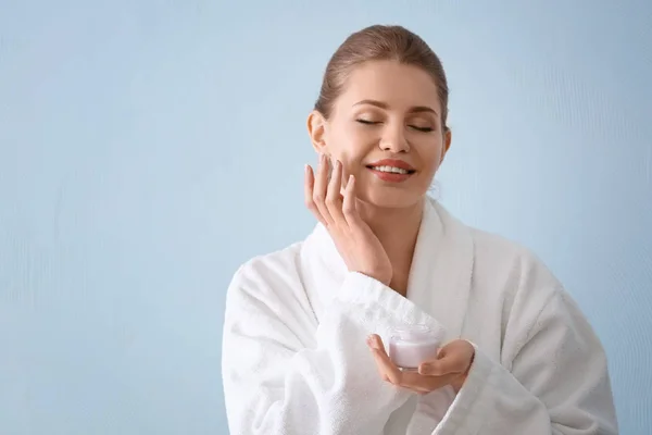 Young woman applying cream onto her skin against color background — Stock Photo, Image