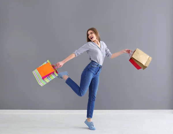 Mulher bonita com sacos de compras contra a parede cinza — Fotografia de Stock