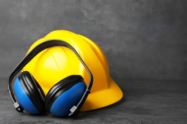 Kopfhörer und Hut auf dem Tisch vor grauem Hintergrund. Gehörschutzausrüstung — Stockfoto