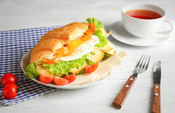 Placa com saboroso sanduíche croissant na mesa — Fotografia de Stock