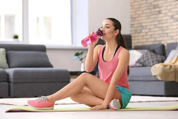 Mooie jonge vrouw drinkbaar water na het doen van fitness oefeningen thuis — Stockfoto