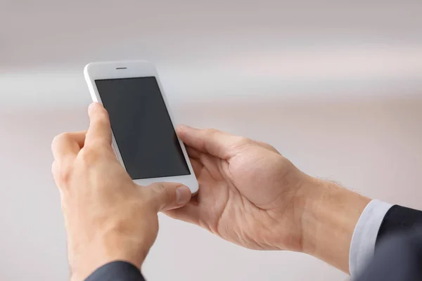 Homem segurando smartphone com tela em branco no fundo embaçado — Fotografia de Stock