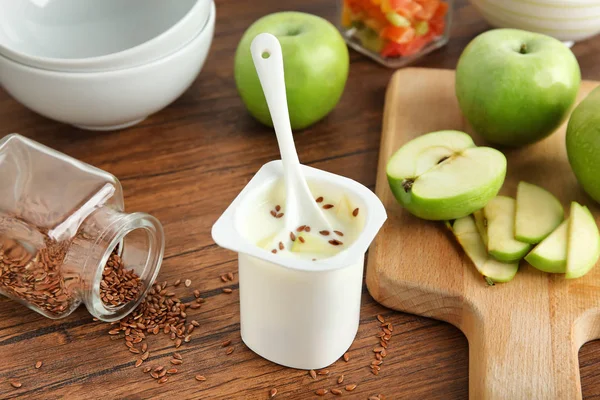 Plastic cup of yummy apple yogurt with flax seeds on wooden table — Stock Photo, Image