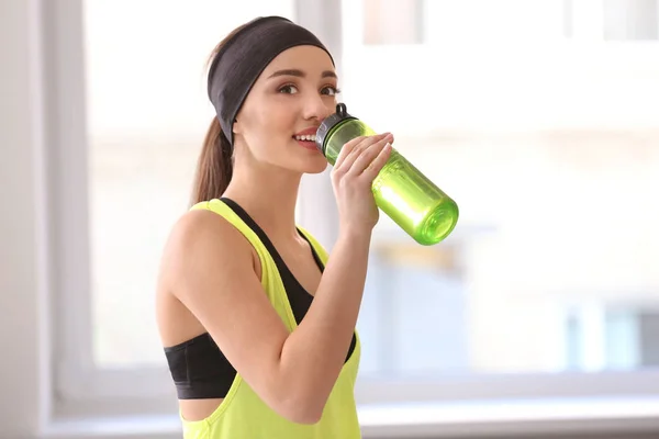 Красивая молодая женщина пьет воду после занятий фитнесом дома — стоковое фото