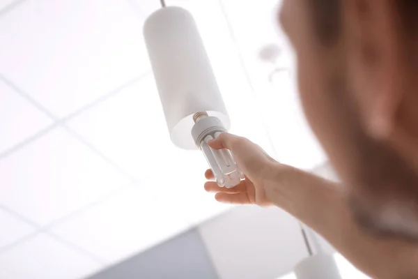 Man van de veranderende gloeilamp in een lamp, binnenshuis — Stockfoto